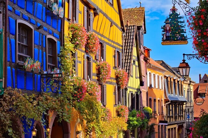 Blue and yellow house fronts hung with geraniums, a decorated fir at the corner
