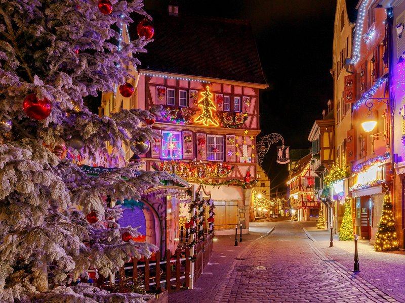 A half-timbered street under Christmas lights after dark