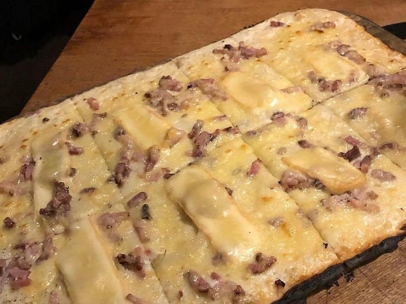 A tarte flambée on its board: cream, onion and bacon on thin dough